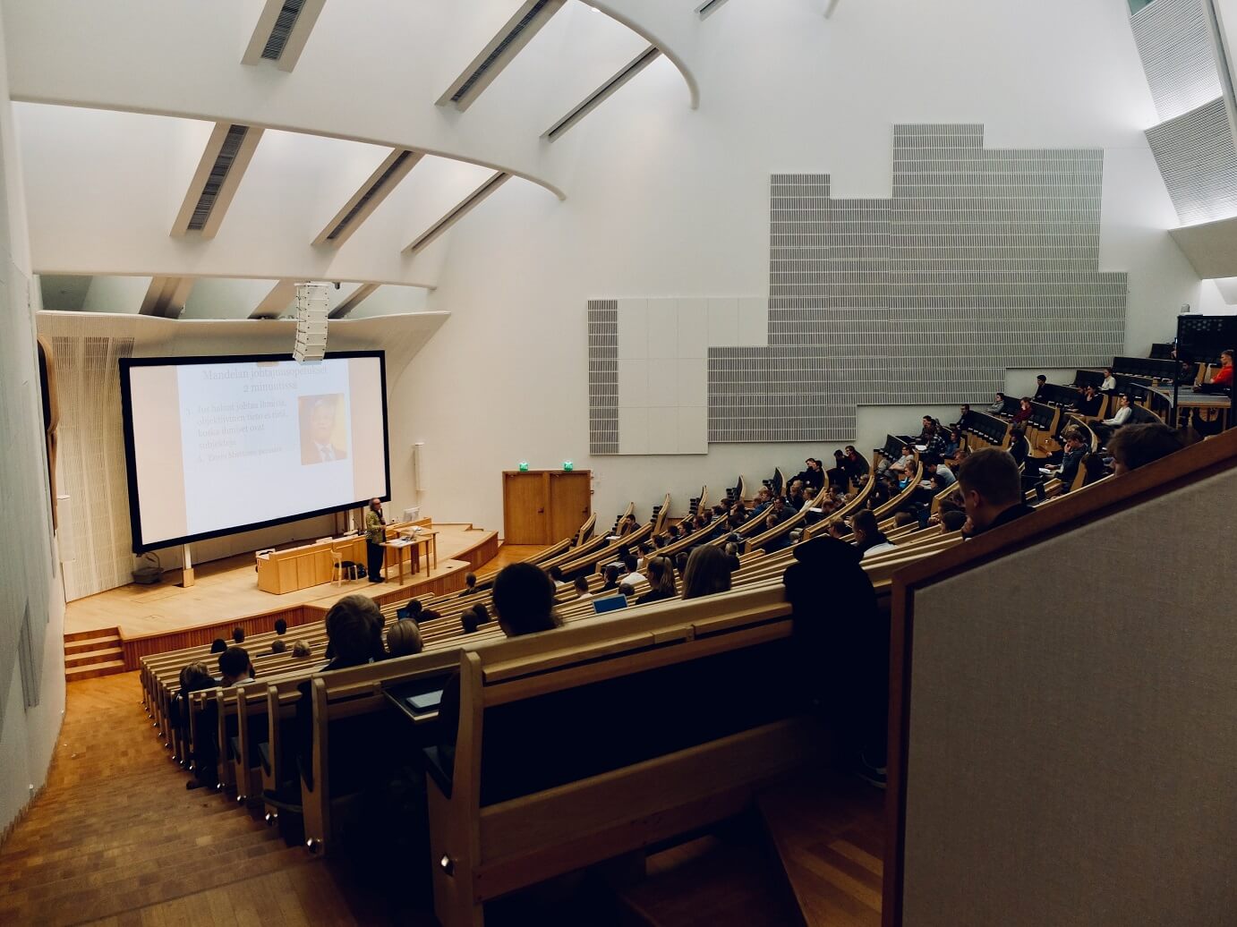 Lecture theatre of scholars sitting in tiered seating in front of a projection screen.