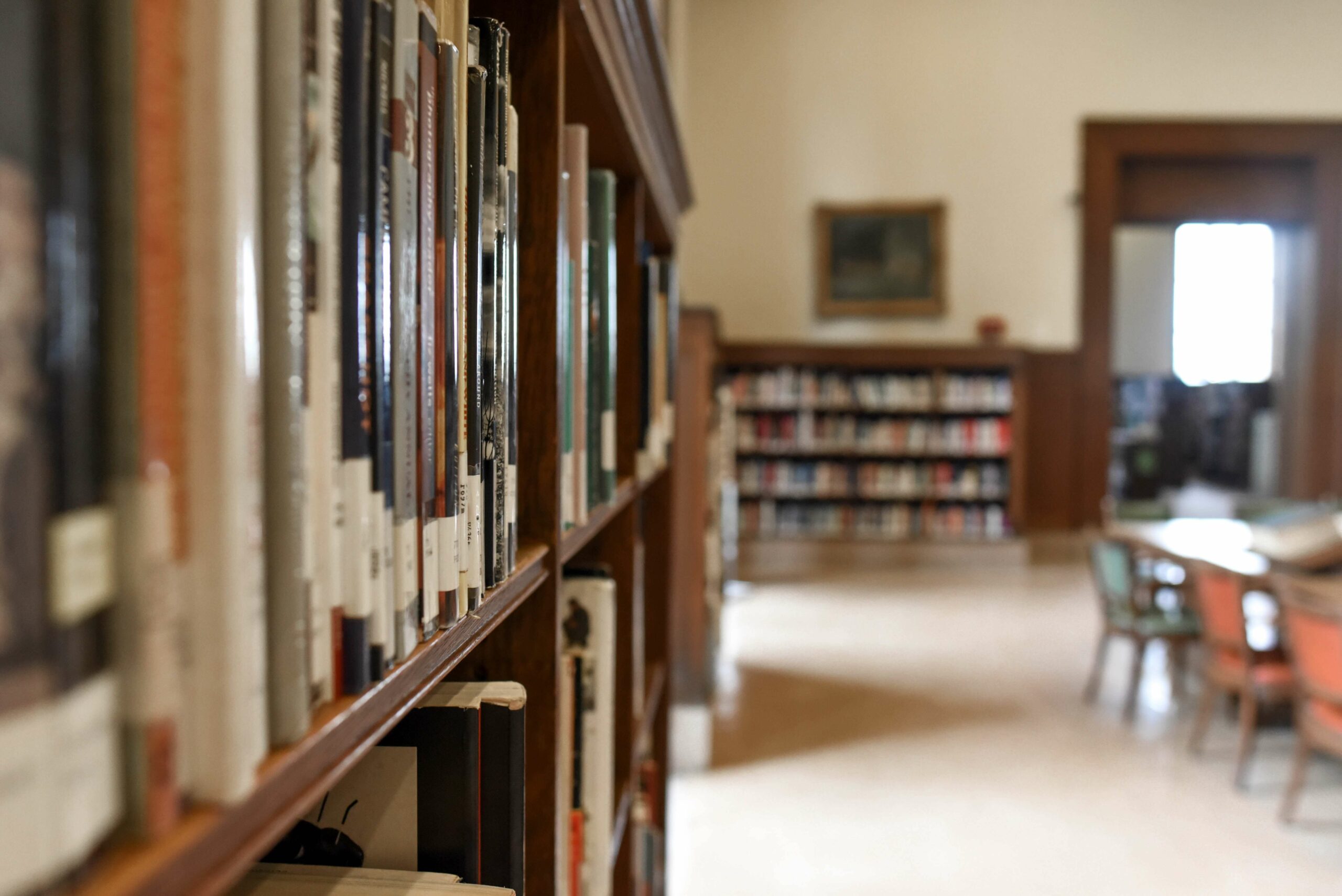 Close up of a book shelf, with a wooden table and chairs to the right.