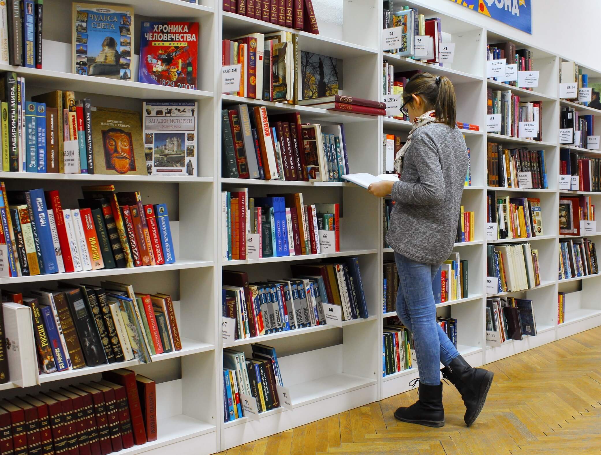 Person standing in front of a bookshelf, reading a book.